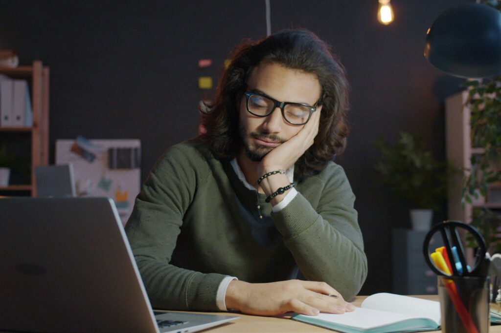 Tired man sitting at his desk with his head in his hand and his eyes closed because he's working too much.