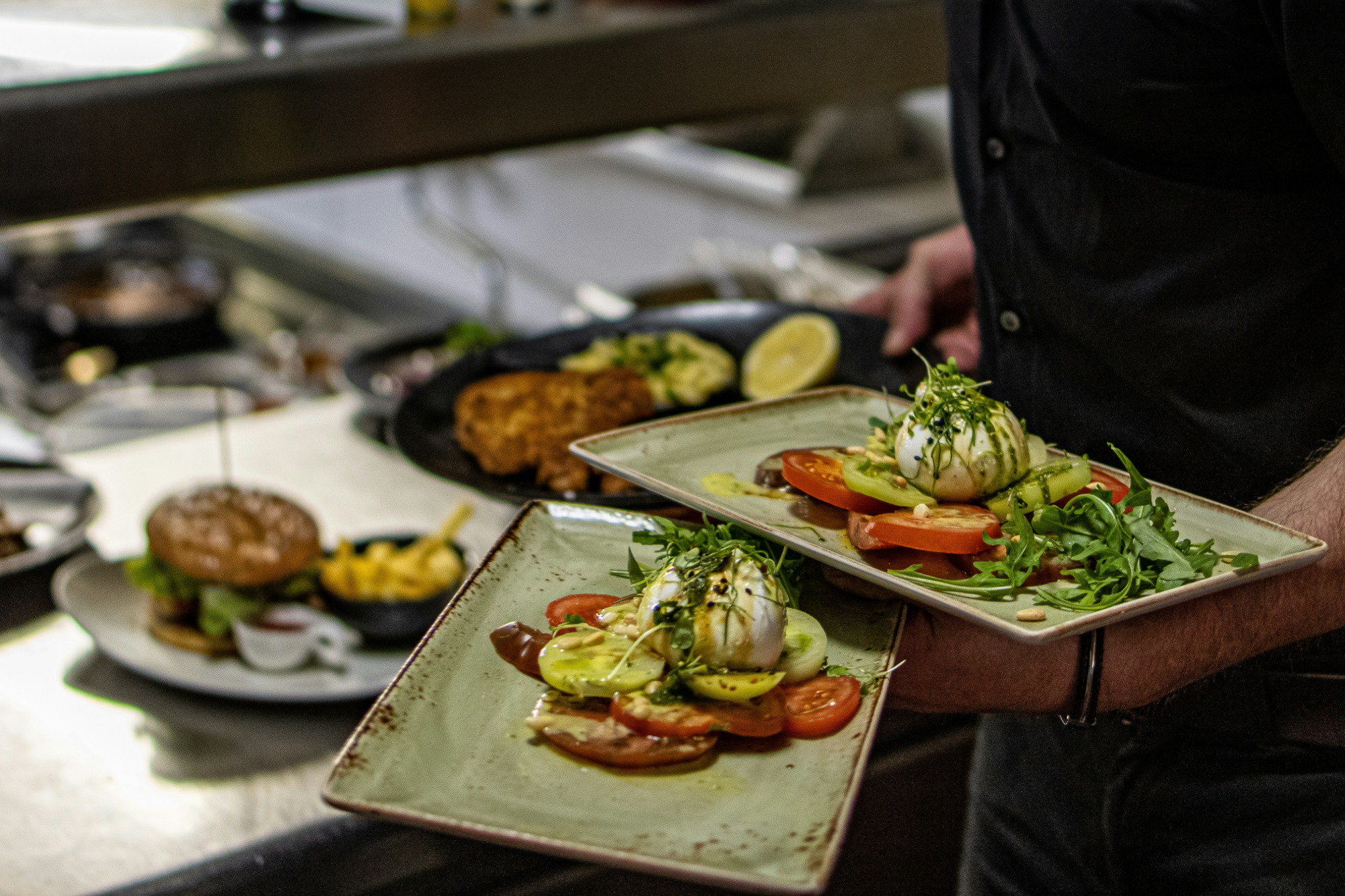Restaurant server picking up plated dishes from the kitchen line.