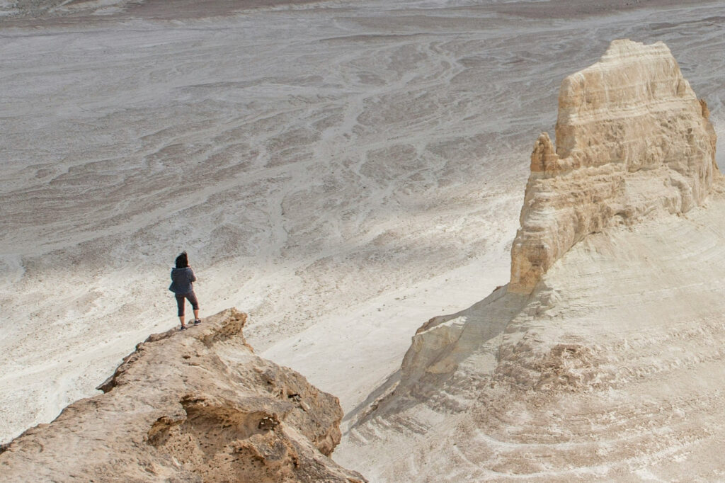 Person standing at the edge of one rock plateau looking across to another in the distance just as a business owner contemplates overcoming a business plateau.